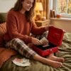 Una joven sentada en su cama usando una caja de caudales roja abierta para guardar fajos de billetes de euro.