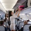 Joven estibando maleta de cabina rigida fucsia en compartimento superior avion MegaShark