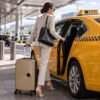 Mujer cargando maleta de cabina rigida dorada en un taxi en la salida del aeropuerto MegaShark
