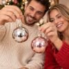 Pareja sonriente mostrando bolas navideñas brillantes a la cámara en MegaSharkCo.
